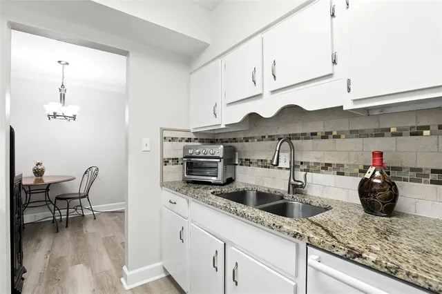 a kitchen with stainless steel appliances granite countertop a sink dishwasher a stove and white cabinets with wooden floor