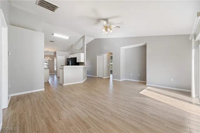 an empty room with wooden floor and kitchen view