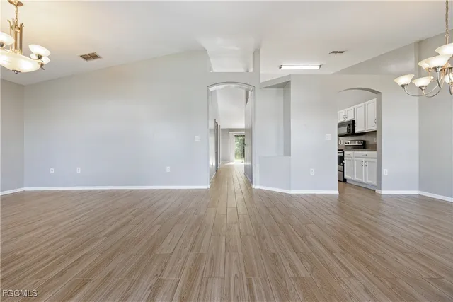 a view of empty room with wooden floor and kitchen