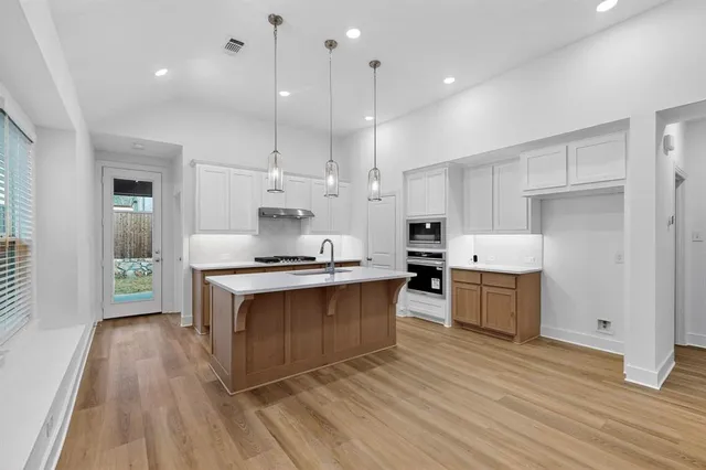 a large kitchen with stainless steel appliances granite countertop a stove a sink dishwasher and a refrigerator with wooden floor