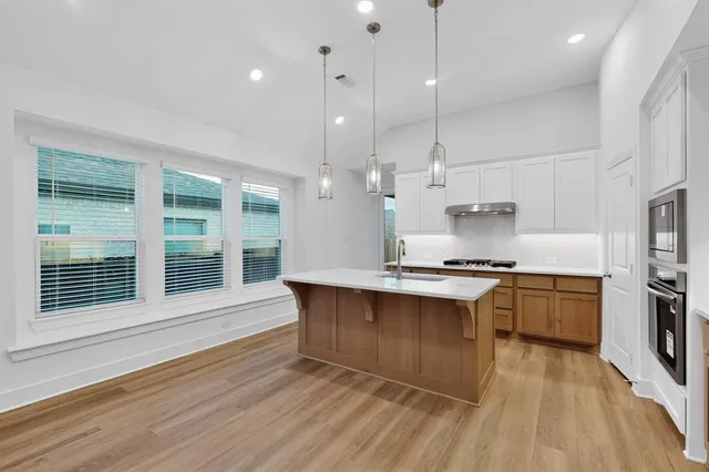 a large kitchen with stainless steel appliances granite countertop a stove a sink dishwasher a refrigerator white cabinets and wooden floor next to a window