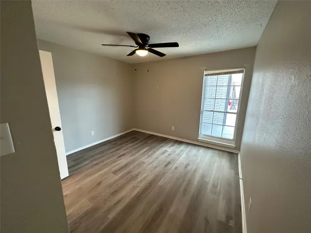 an empty room with wooden floor fan and windows