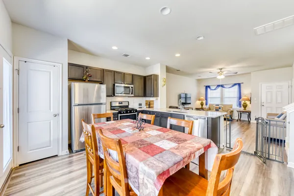 a kitchen with stainless steel appliances kitchen island granite countertop a refrigerator a stove top oven and a dining table with wooden floor