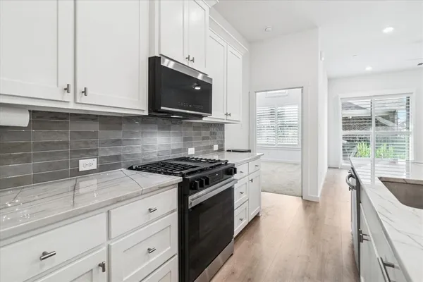 a kitchen with stainless steel appliances granite countertop white cabinets and a stove top oven