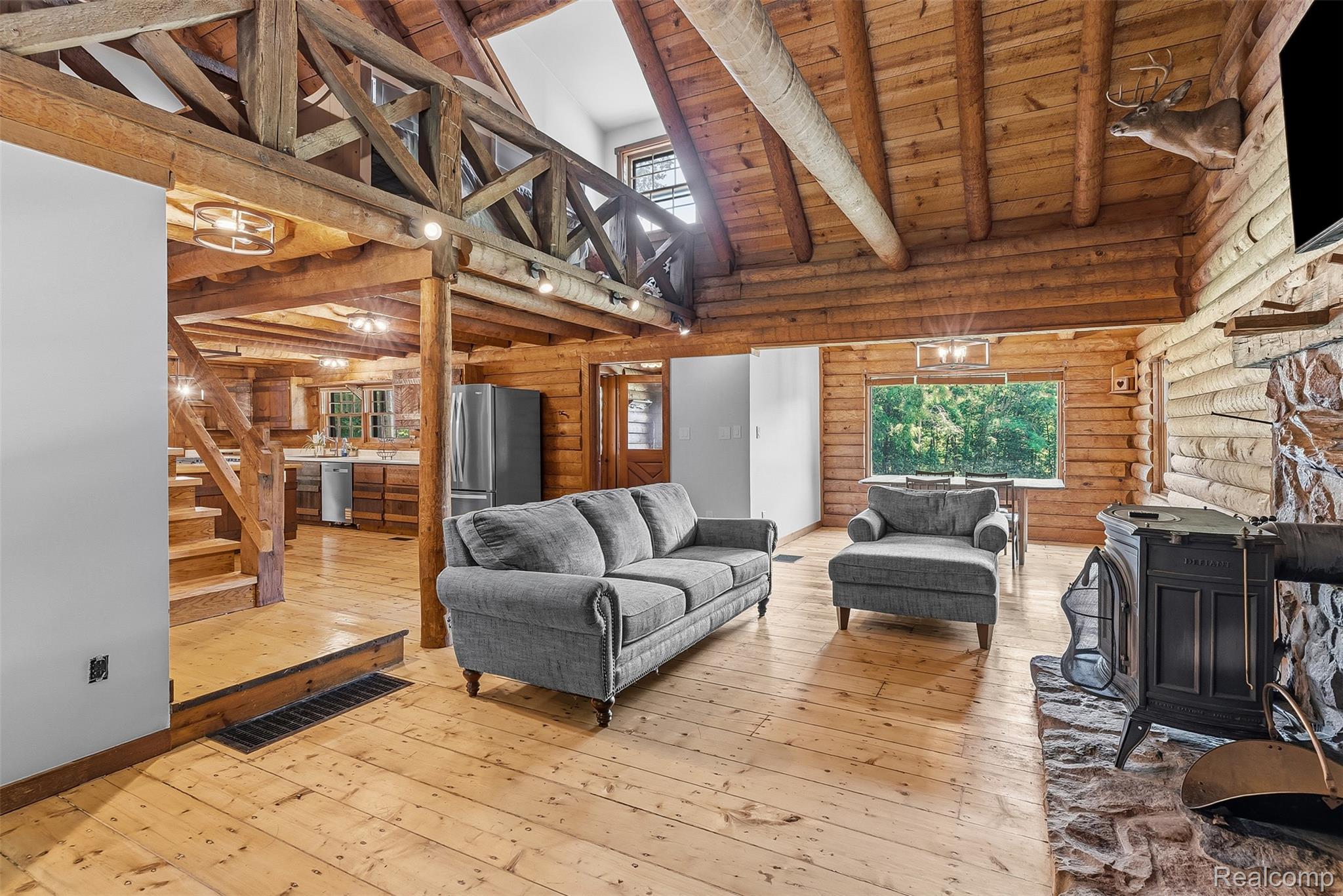 3656 Stanley Road Columbiaville, MI 48421 - Photo 5 of 65 Expansive great room featuring a wood-burning stove with stone surround, natural wood-finish flooring, and exposed log walls