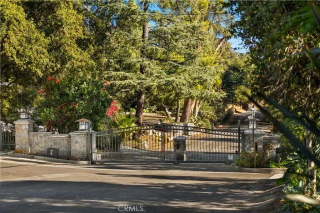 a view of a brick house with large trees and wooden fence
