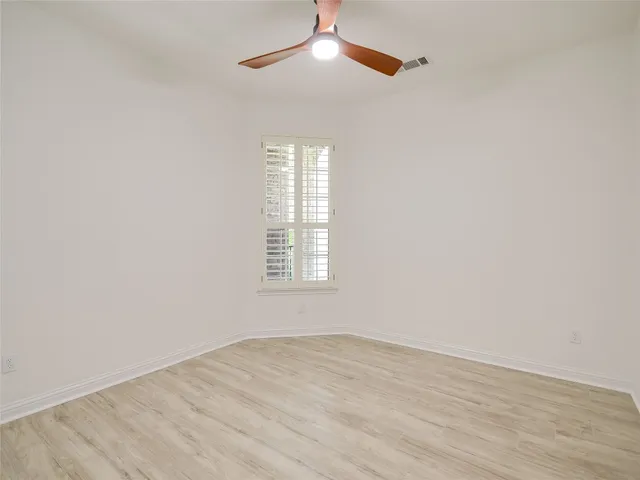 an empty room with wooden floor chandelier fan and windows