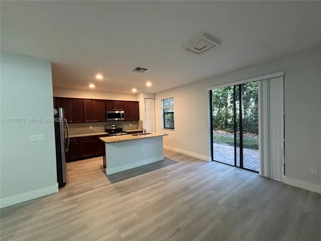 a kitchen with stainless steel appliances kitchen island granite countertop a refrigerator a sink dishwasher a stove and a dining table with wooden floor