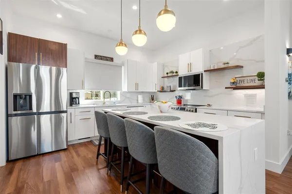 a kitchen with stainless steel appliances granite countertop a refrigerator a sink a stove a microwave and white cabinets with wooden floor