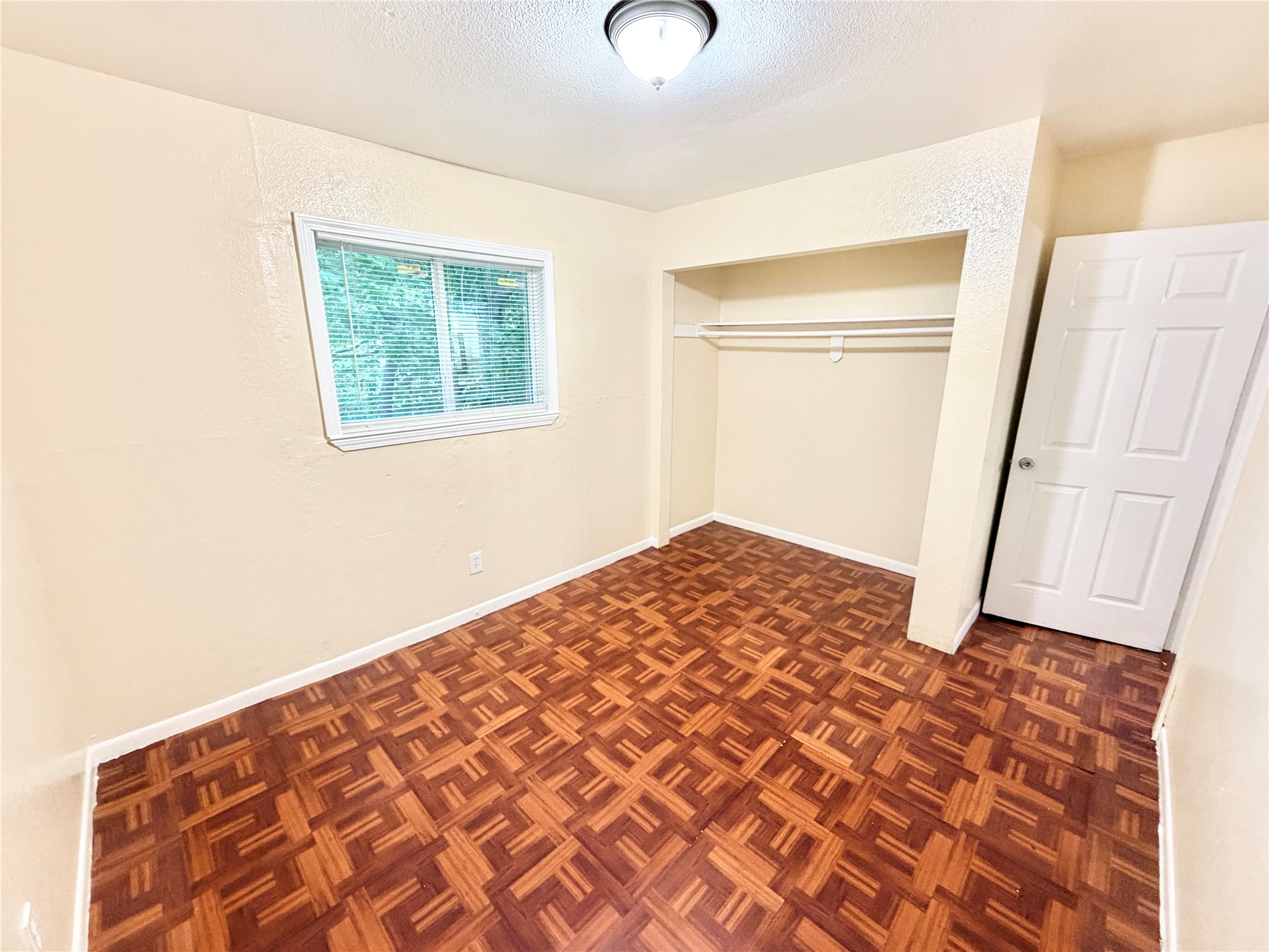 6257 Manor Road, Unit B Austin, TX 78723 - Photo 33 of 38 Interior room featuring patterned wood-finish flooring, a window with white trim, a built-in closet with shelving and hanging rod, a white paneled door, and a ceiling-mounted light fixture