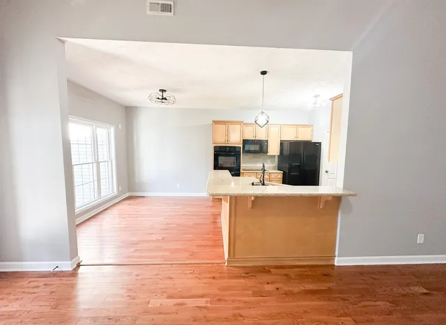 a view of a living room with kitchen island stainless steel appliances wooden floor and window