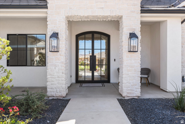 1192 East Corral Way Washington, UT 84780 - Photo 8 of 81 Stucco exterior featuring stacked stone columns, a double arched glass-paneled entry door, and two black wall-mounted lantern lights