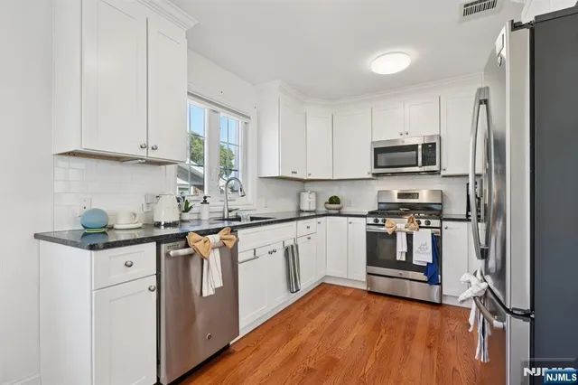 a kitchen with stainless steel appliances granite countertop a stove top oven a sink and dishwasher a refrigerator with wooden floor