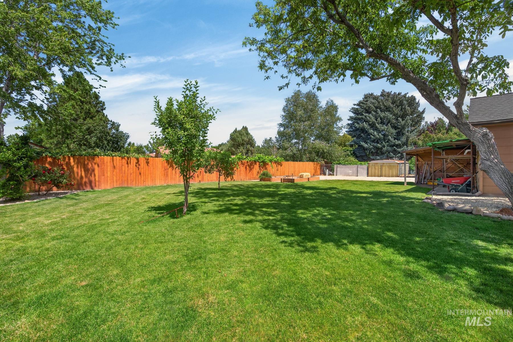 9622 Delaware Street Boise, ID 83709 - Photo 38 of 48 Expansive backyard featuring a lush lawn, mature trees, a wooden privacy fence, and an outdoor storage structure