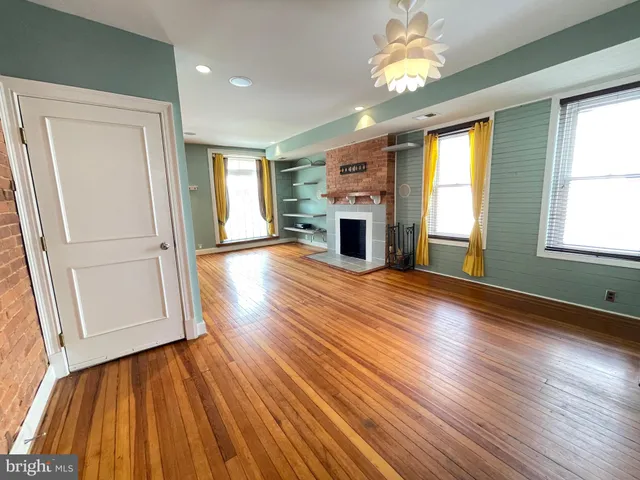 an empty room with wooden floor fireplace and windows