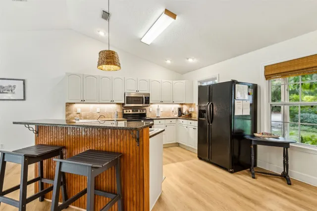 a kitchen with stainless steel appliances kitchen island granite countertop a refrigerator a stove a sink a dining table and chairs with wooden floor