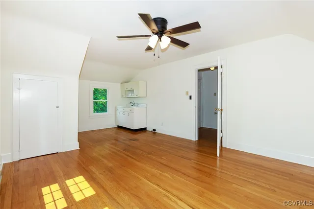 a view of an empty room with wooden floor and a ceiling fan
