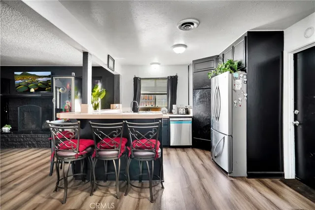 a kitchen with stainless steel appliances kitchen island granite countertop a refrigerator a microwave oven a dining table and chairs with wooden floor