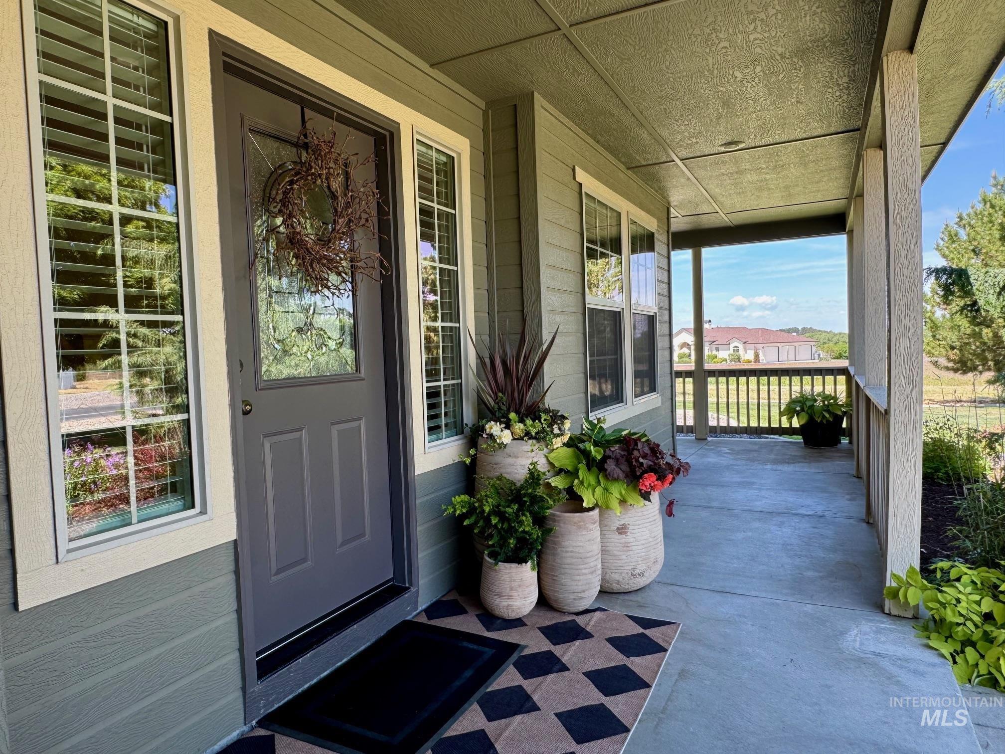 9299 Kemp Road Middleton, ID 83644 - Photo 40 of 50 Covered front porch featuring a dark gray entry door with decorative glass, two side windows with horizontal blinds, and a concrete floor