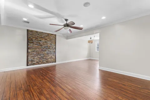 a view of an empty room with wooden floor and a ceiling fan
