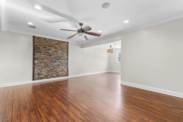 a view of an empty room with wooden floor and a ceiling fan