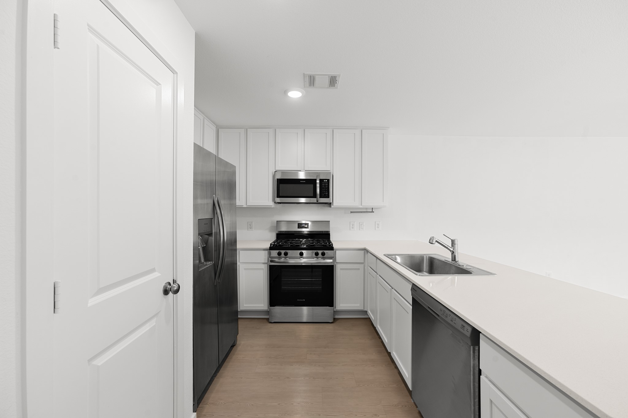 252 Houston Street Angleton, TX 77515 - Photo 7 of 49 Another view highlights the kitchen’s efficient layout with white cabinetry, stainless steel appliances, recessed lighting, and ample countertop workspace.