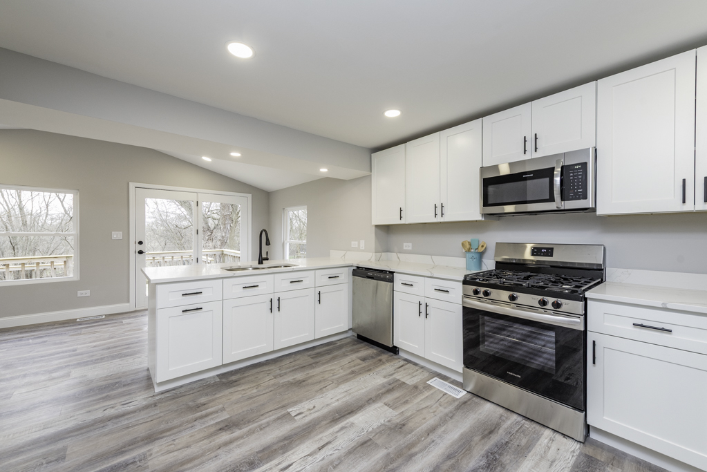 24199 West Beach Grove Road Antioch, IL 60002 - Photo 3 of 22 a kitchen with granite countertop white cabinets a sink a stove a microwave and wooden floors