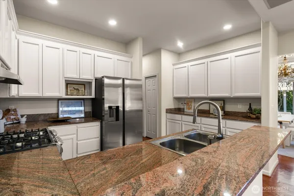 a kitchen with granite countertop a refrigerator a sink a stove and white cabinets