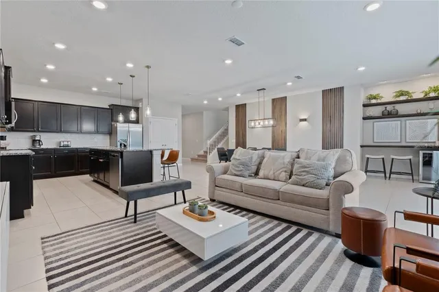 a living room with stainless steel appliances furniture a rug kitchen view and a table