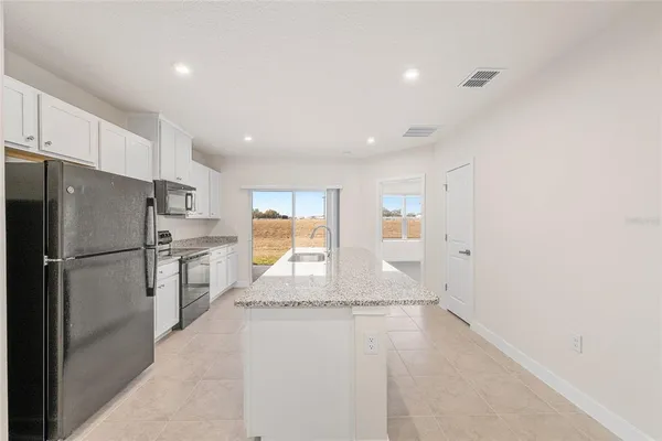 a kitchen with granite countertop a refrigerator a sink and white cabinets