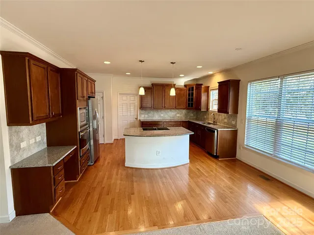 a kitchen with stainless steel appliances kitchen island granite countertop wooden cabinets a stove a sink and a large window