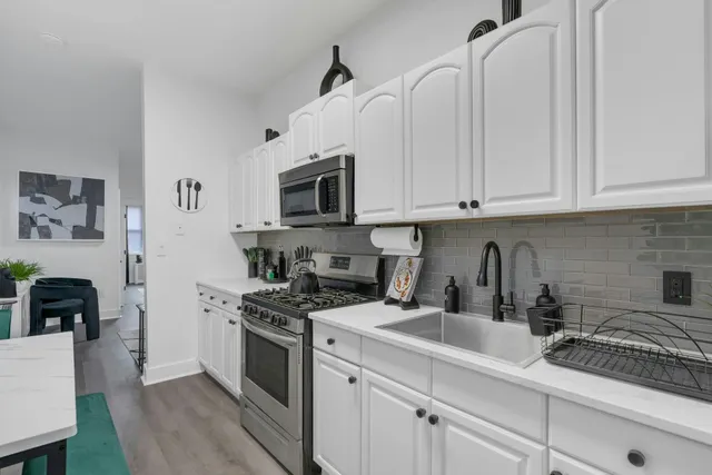 a kitchen with stainless steel appliances granite countertop white cabinets a sink a stove a microwave and a refrigerator