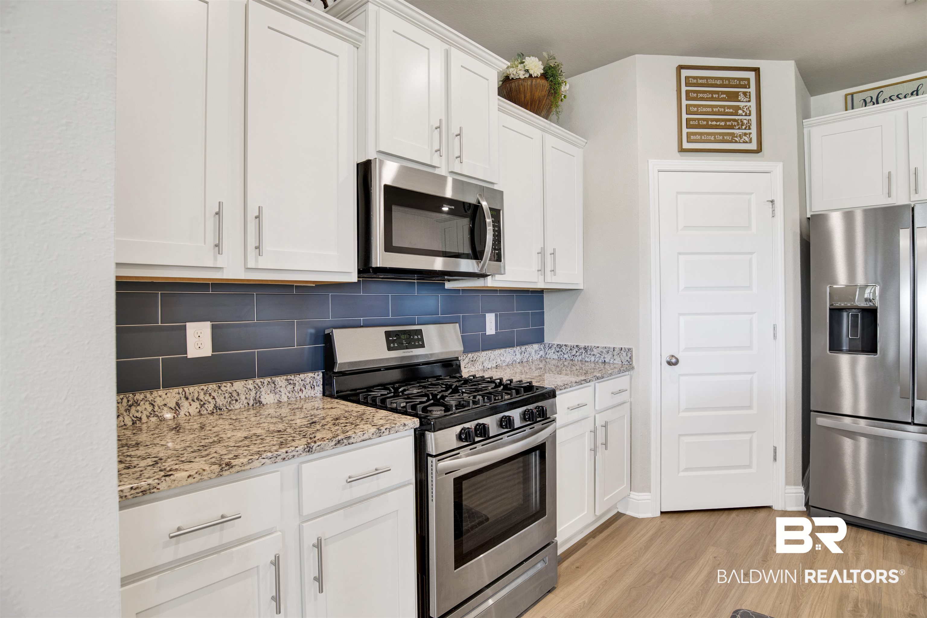 9431 Swan Point Road Daphne, AL 36526 - Photo 10 of 35 Kitchen with stainless steel appliances, light wood-style flooring, white cabinetry, decorative backsplash, and light stone countertops