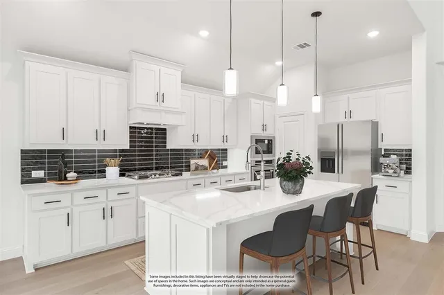 a kitchen with stainless steel appliances kitchen island granite countertop a sink a stove a refrigerator and white cabinets with wooden floor