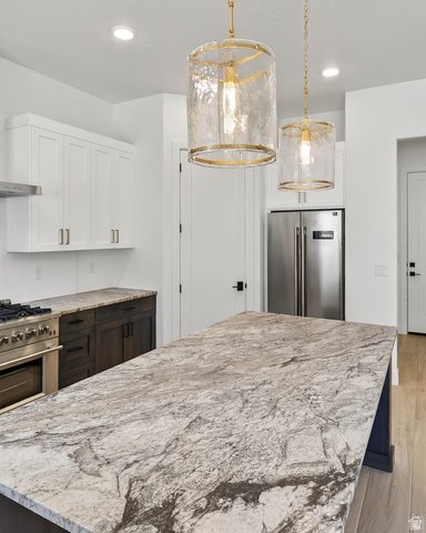 2862 South Mountain Rnch Road Cedar City, UT 84720 - Photo 13 of 64 Kitchen island with a patterned stone countertop, two pendant light fixtures, white upper cabinetry, dark lower cabinetry, and stainless steel appliances