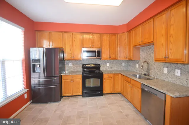 a kitchen with granite countertop stainless steel appliances a refrigerator stove top oven and sink