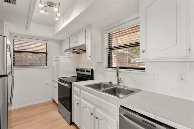 a view of a kitchen with a sink and dishwasher a refrigerator with white cabinets
