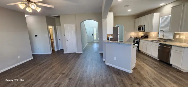 a kitchen with stainless steel appliances granite countertop a refrigerator a sink dishwasher a stove and white countertops with wooden floor