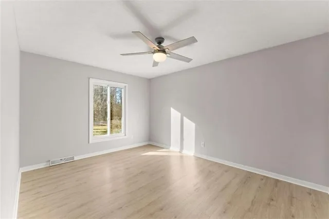 an empty room with wooden floor fan and windows