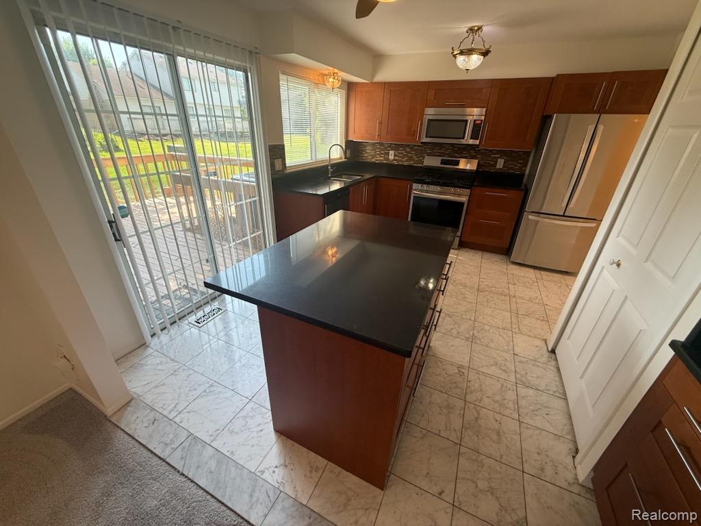 28144 Yorktown Road Farmington, MI 48331 - Photo 7 of 25 Kitchen featuring a large central island with a dark countertop, stainless steel appliances, wood cabinetry, and a patterned tile backsplash