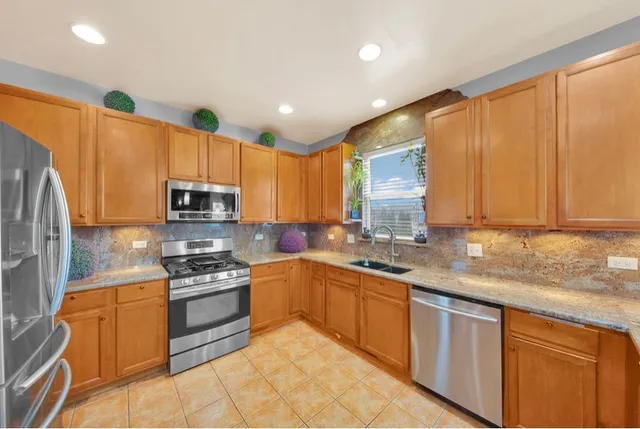 a kitchen with stainless steel appliances granite countertop a sink a stove a refrigerator cabinets and a window