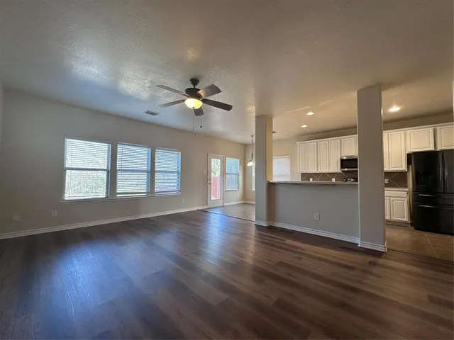 an empty room with wooden floor and kitchen view