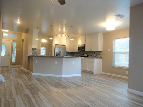 a kitchen with granite countertop a stove a sink a refrigerator wooden floor and cabinets