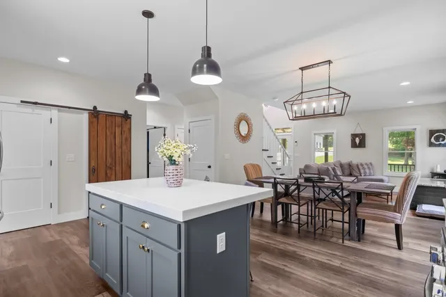 a kitchen with stainless steel appliances granite countertop a stove top oven a refrigerator a kitchen island a dining table and chairs with wooden floor