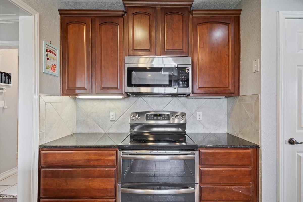 8600 Five Wells Road Rogers, TX 76569 - Photo 13 of 40 Kitchen with appliances with stainless steel finishes, dark stone countertops, a textured wall, and tasteful backsplash