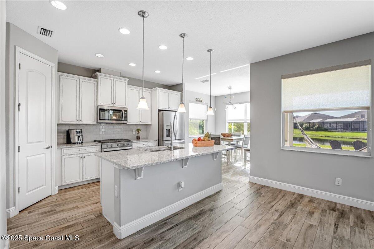3379 Ribbon Grass Drive Melbourne, FL 32940 - Photo 24 of 62 a kitchen with stainless steel appliances a stove top oven a sink a refrigerator and white cabinets with wooden floor