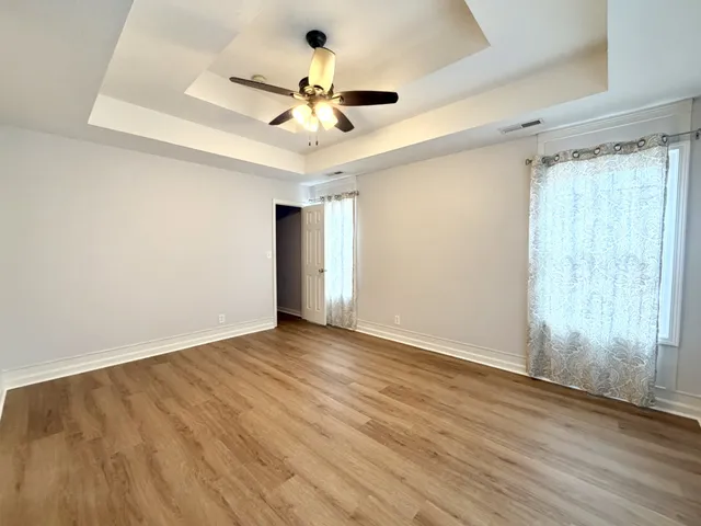 a view of an empty room with wooden floor and a ceiling fan