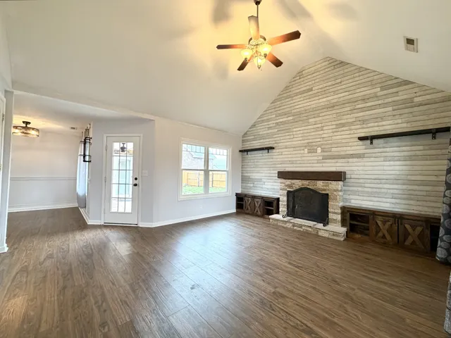 a view of an empty room with wooden floor fireplace and a window