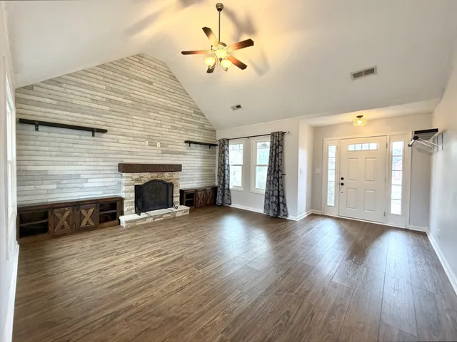 an empty room with wooden floor fireplace and windows