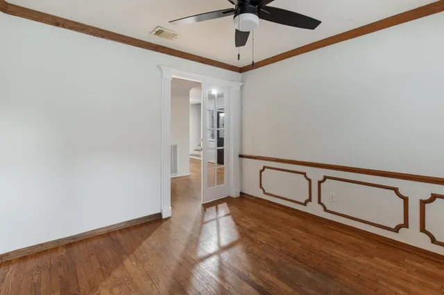 a view of an empty room with wooden floor and a ceiling fan